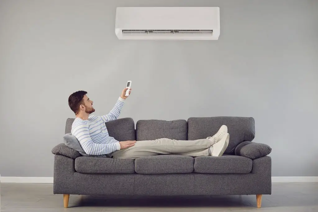 Man sitting on a couch adjusting his air conditioning with a remote control