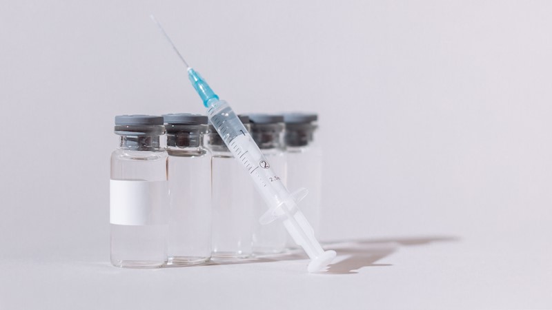 A needle syringe resting upright against 5 vials.