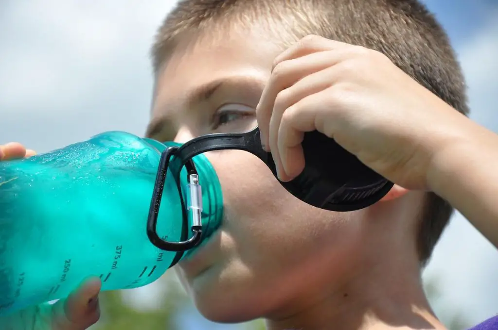 boy outside drinking ice water from a teal water bottle.
