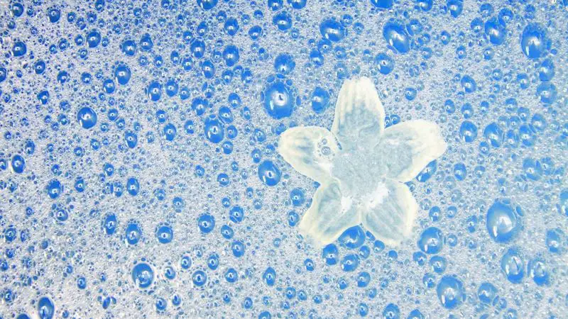 Many bubbles and suds from soap, over a blue background.