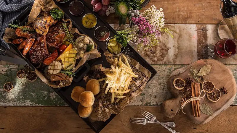 A large tray of buffet style food to include french fries, grilled meats, and vegetables.