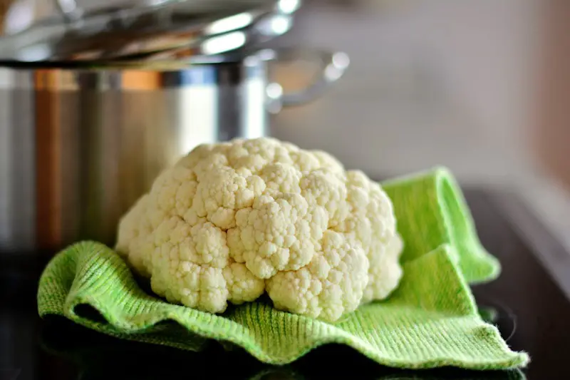A head of cauliflower outside of a pot, sitting on a green kitchen towel.