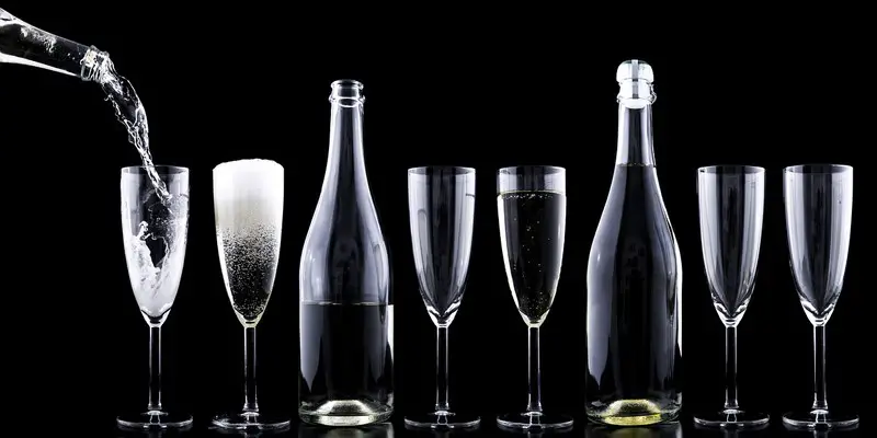 six champagne glasses being filled by two bottle of alcohol.