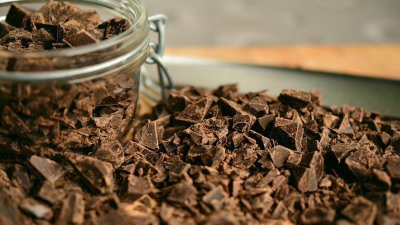 A jar full of shaved and chunked chocolate with chocolate also surrounding the jar.