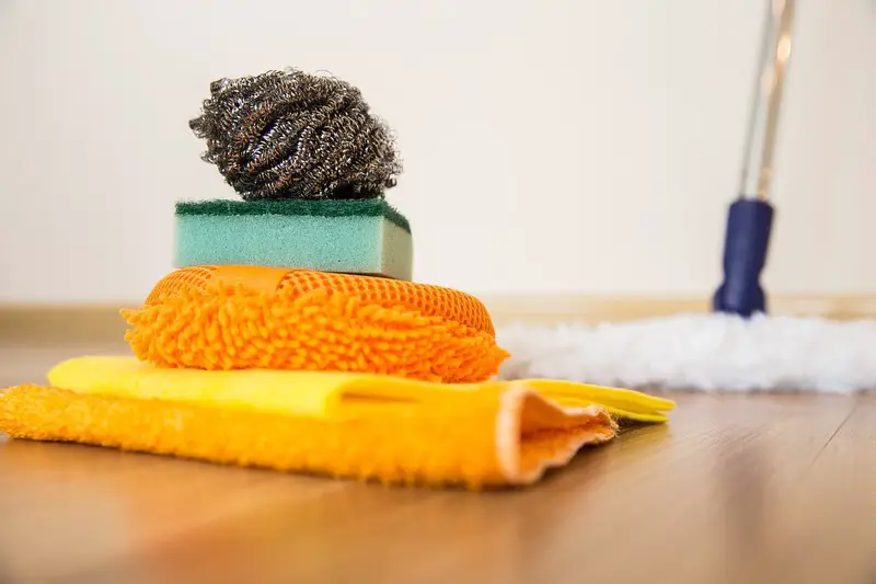 a pile of cleaning supplies of rags and sponges with a mop in the background.