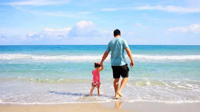 Father and daughter walking through the waves at the beach on a sunny day.