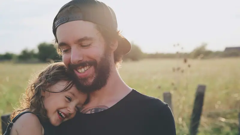A father with his daughter in his arms. They are happy outside in a field.