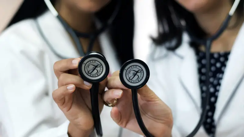 Two female doctors holding up stethoscopes.