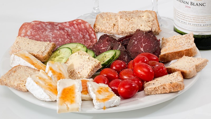 A plate full of meats, cheeses, tomatoes, with a bottle of south African wine.