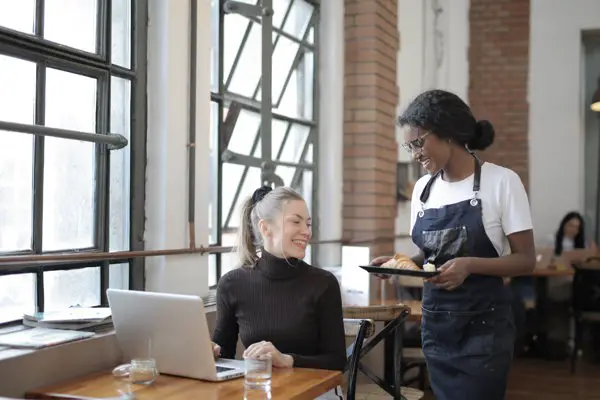 waiter bringing out food to woman on laptop