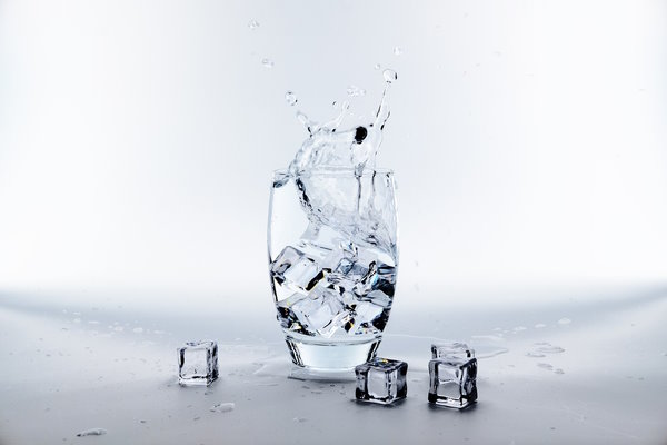 glass of water with ice being dropped into it and splashing.