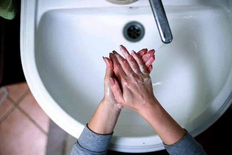 A woman washing her hands with soap and water, over a white ceramic sink.