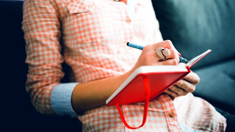 Person with a large ring on their finger, writing in a journal or diary with a blue pen.