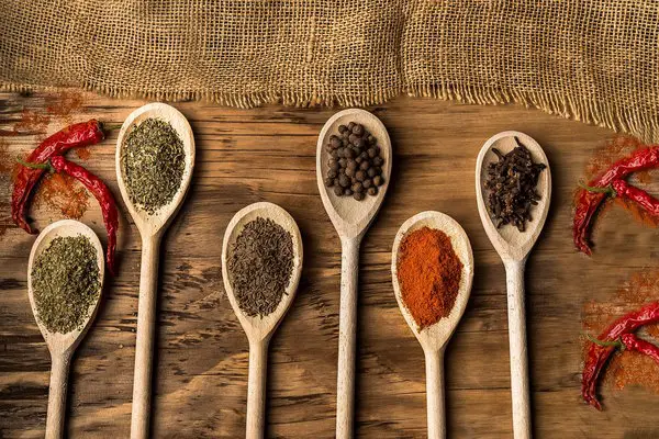 Six wooden spoons filled with various spices and herbs.