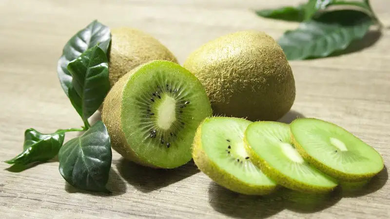 whole and cut kiwi on a wooden table.