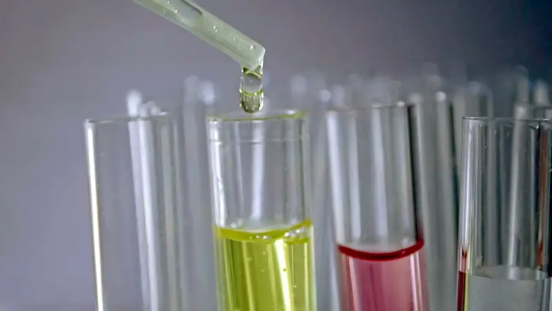 Multiple lab test tubes with various colors of liquid in them. A dropper is putting fluid into the yellow fluid-filed tube.