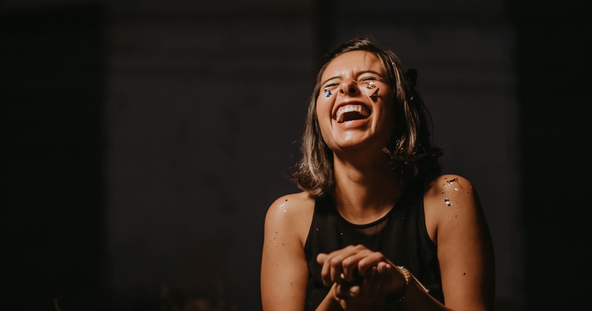 Woman laughing with hands together with glitter on her face and shoulders.