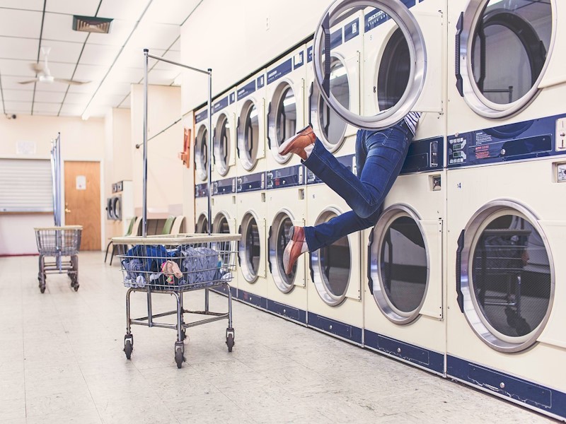 Woman getting clothes out of the top dryer in a laundry mat, with a basket of clean clothes behind her.