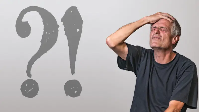 A confused man in a black shirt, who is holding his head, and his eyes are closed.