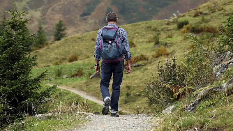 Man walking on a trail in the mountains with a backpack.