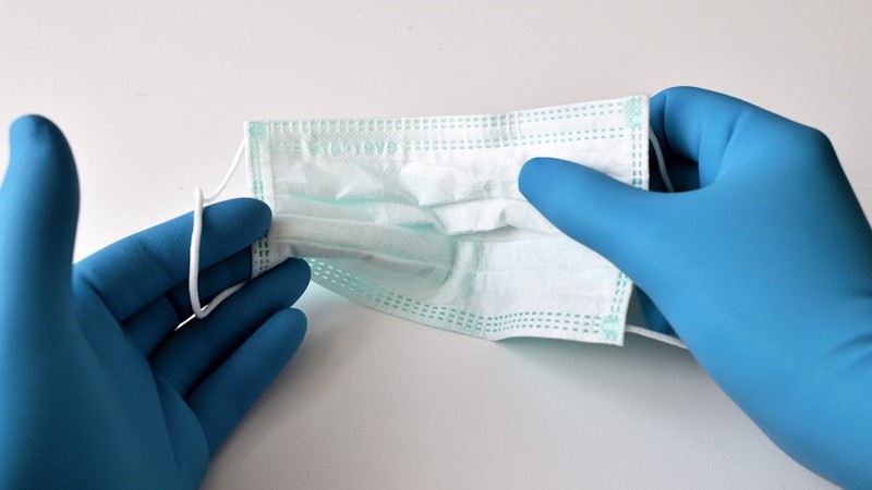 A disposable face mask being held by someone wearing blue surgical gloves.