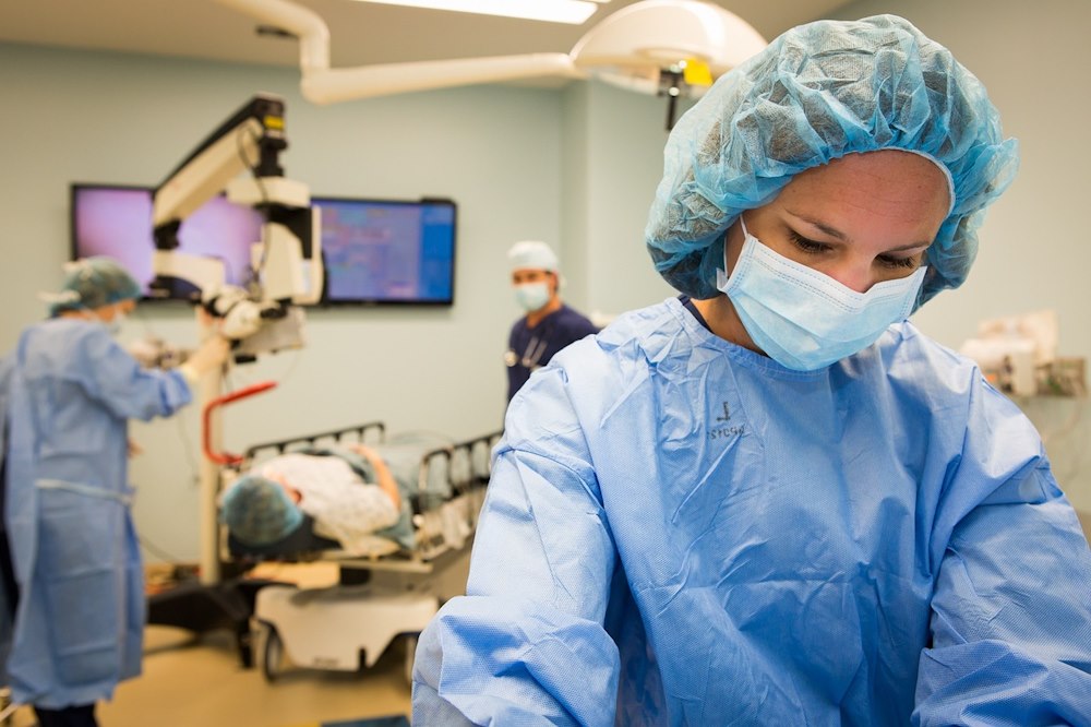 Doctors and nurses prepping a patient for a medical procedure. The medical staff are in blue gowns with medical masks on their faces.