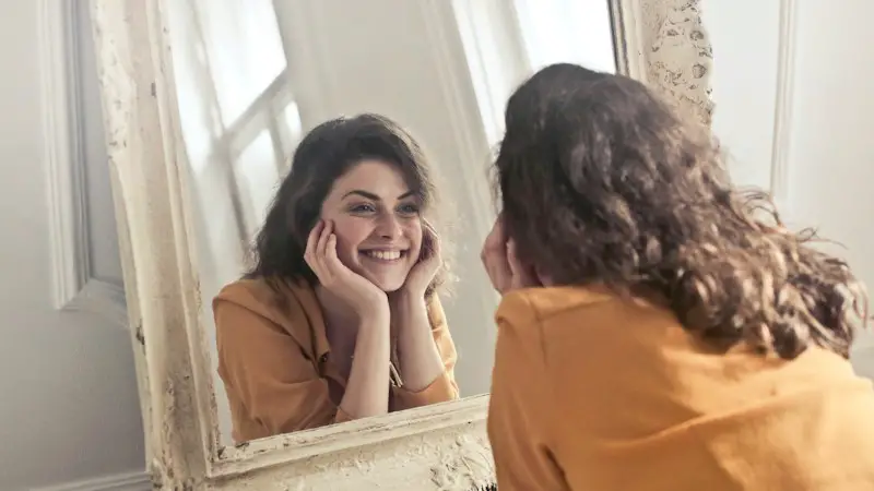 A woman in an orange shirt looking into a mirror.
