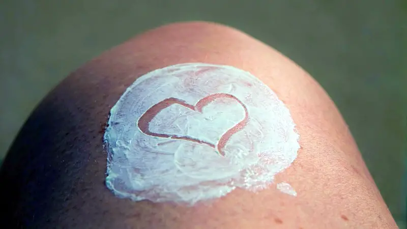 A knee with white moisturizer on it that is not rubbed in. The person has made a heart shape inside of the cream.