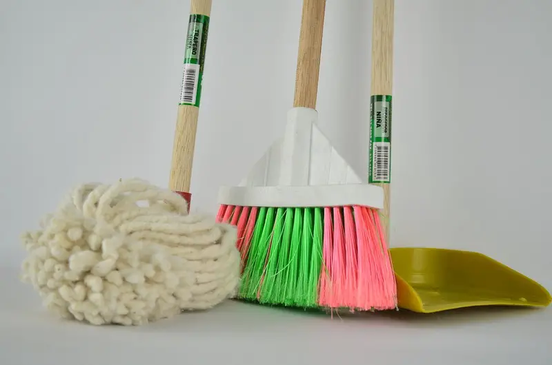 A dry mop, pink and green broom, and a yellow dust pan with wooden handles.