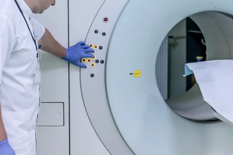 Image of an MRI or CAT scan technician starting the medical imaging machine. The technician is wearing a white lab coat and blue medical gloves.