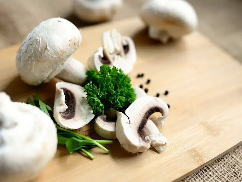 Cutting board with whole and chopped white mushrooms.