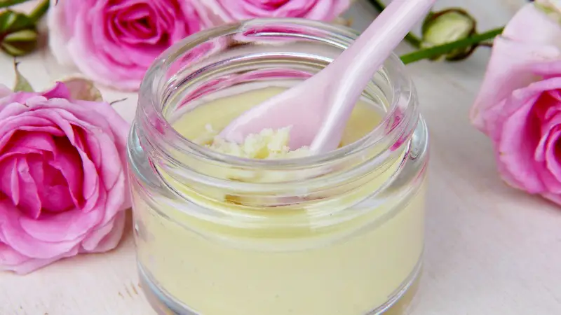 A jar of natural skin moisturizer with roses in the background.