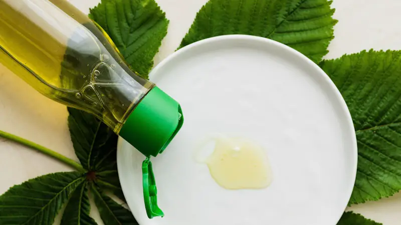 A white plate is resting on a plant leaf, and a natural oil is being poured out onto the plate.