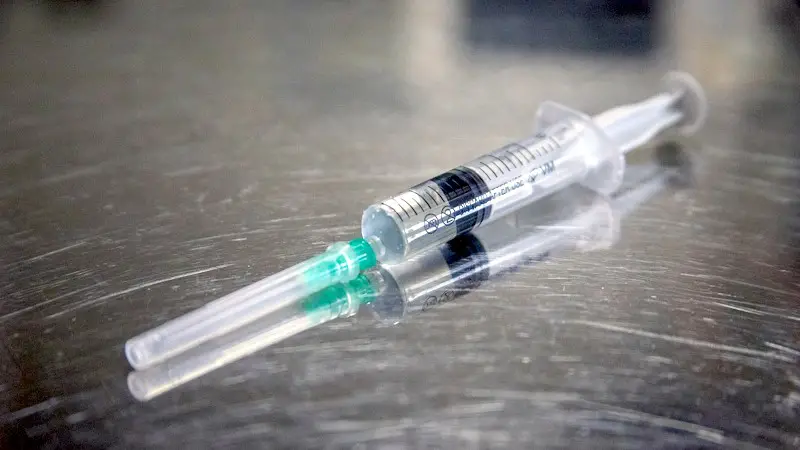A medical syringe and needle on a stainless steel table.