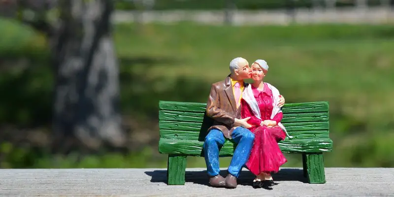 A ceramic figurine of an older couple sitting on a green bench in the park.