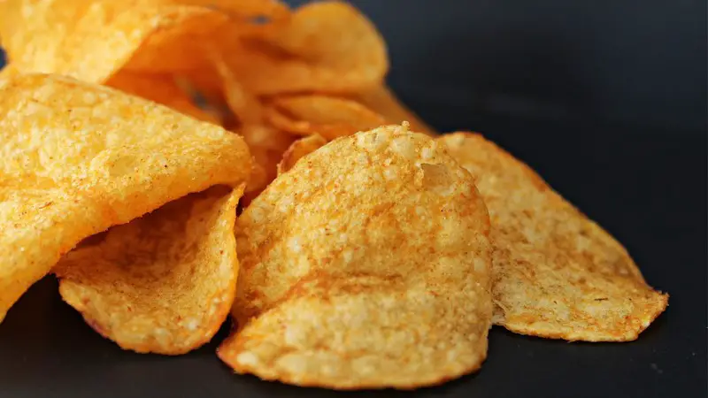 A few crispy potato chips on a black surface.