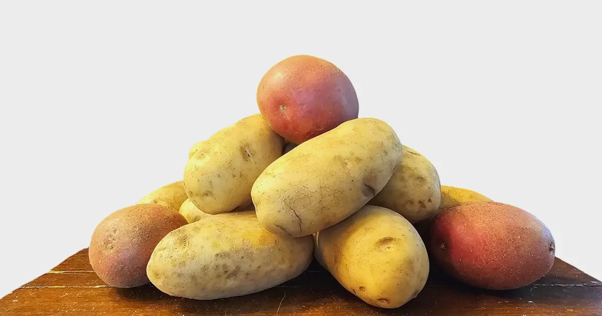 Brown table with a stack of red and russet potatoes with a white background.