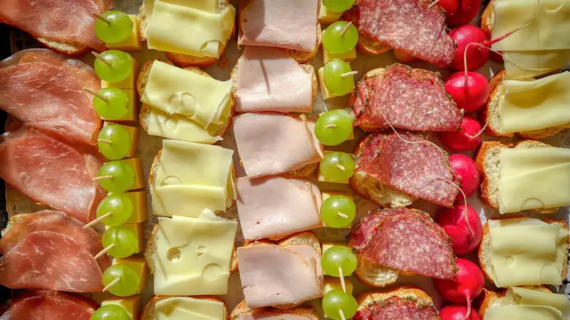 a large spread of bread, lunchmeats, cheeses, and grapes on a platter.