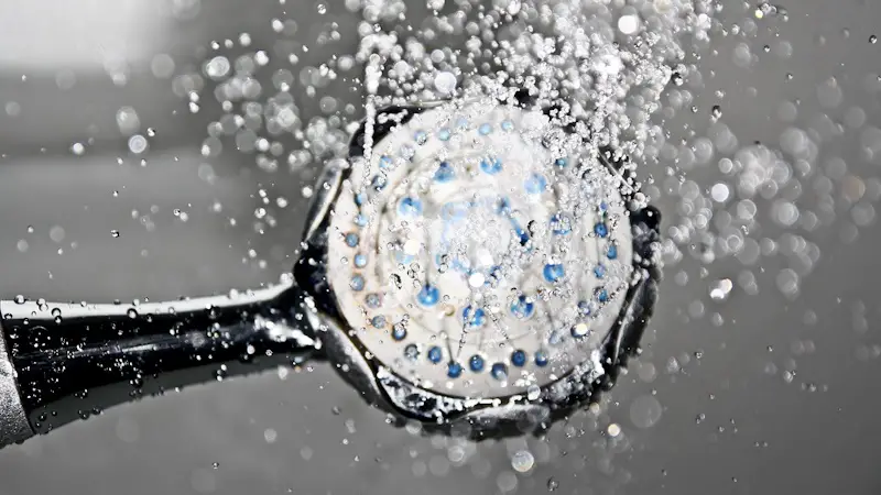 A shower head with the water on. The water is ice-like, with blue color.