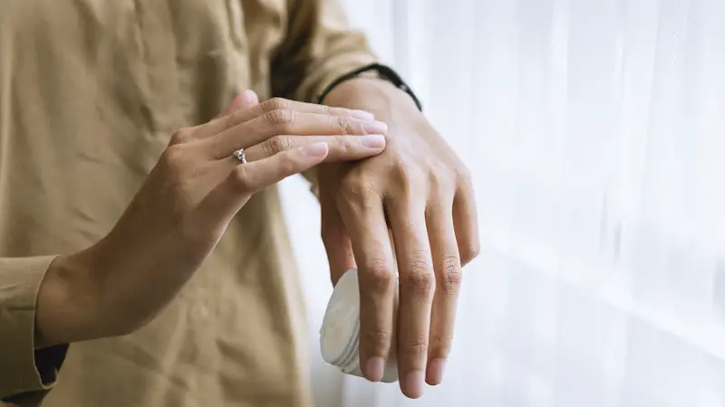 Woman applying moisturizing cream on the top of her hand.