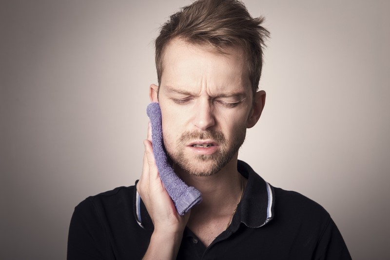 A man in pain holding a warm washcloth to his face. His pain is being caused by his tooth.