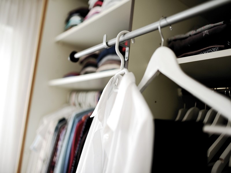 A white shirt hanging in a closet. which is filled with various clothes.