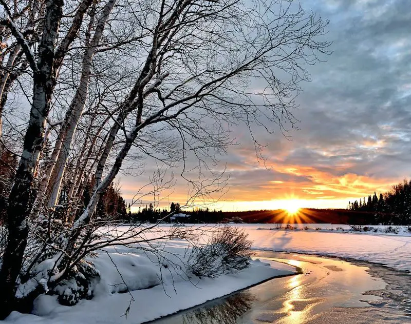 Sun setting on a snowy riverbank in winter.
