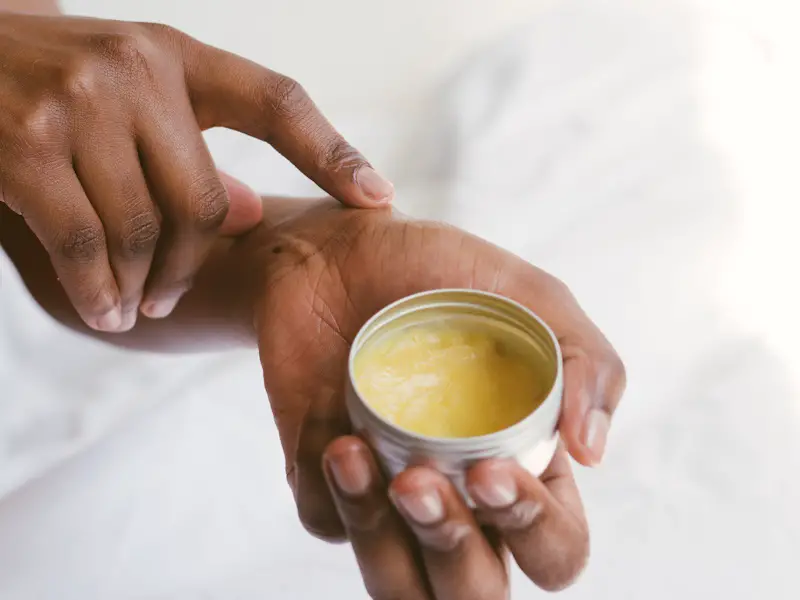 a woman applying a cream onto her skin from a tin of balm