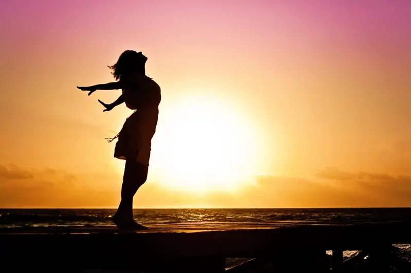 woman standing in the water during sunset, feeling the breeze beneath her arms.