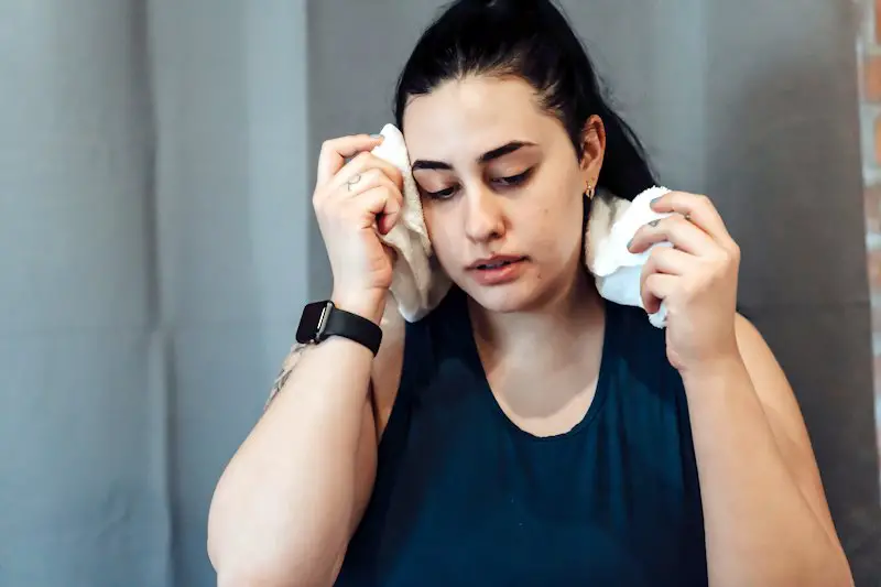 Woman who is sweaty and is using a towel to wipe the sweat from her face.