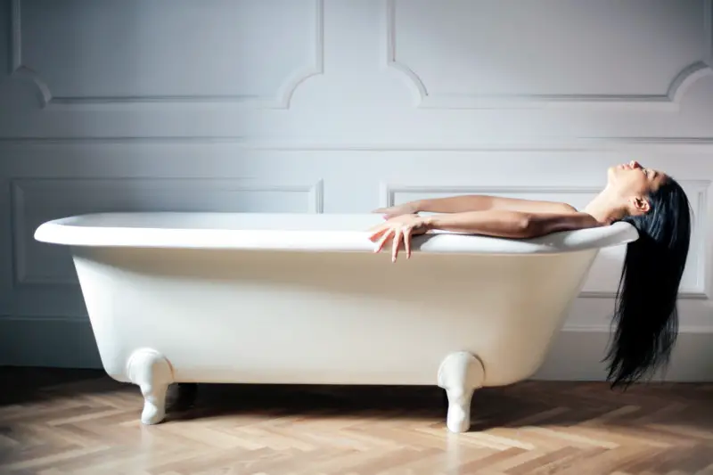 woman laying in a bath with her hair hanging out of the tub.