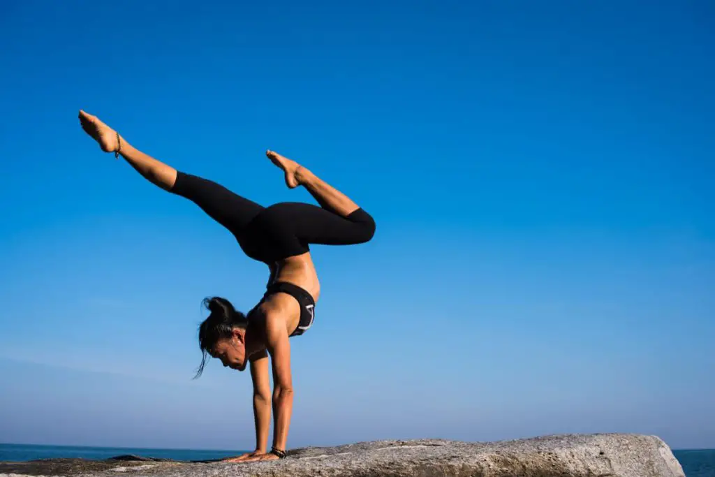 woman performing a yoga handstand on top of a rock ledge