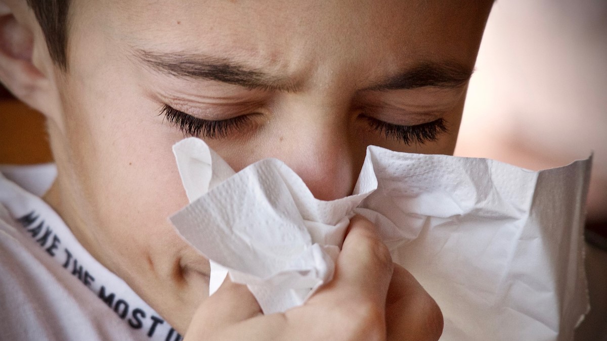 Boy blowing his nose into a tissue with his eyes closed from allergies.