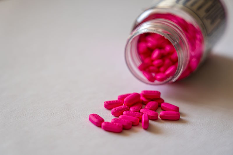 pink pills on a flat surface, next to the open medication bottle